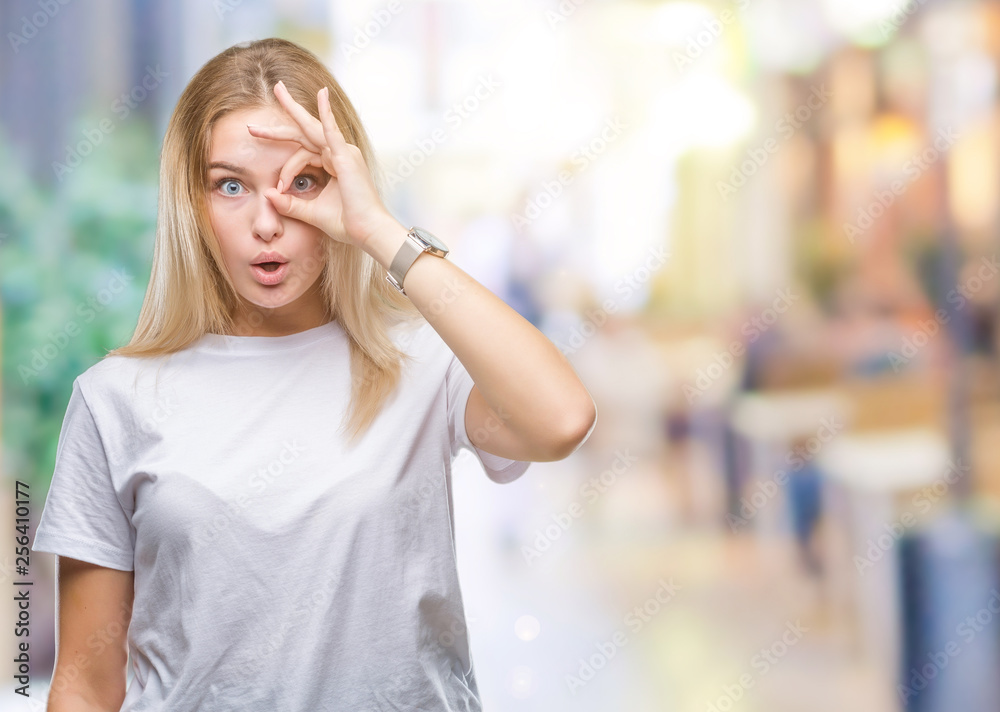 Young caucasian woman over isolated background doing ok gesture shocked with surprised face, eye looking through fingers. Unbelieving expression.