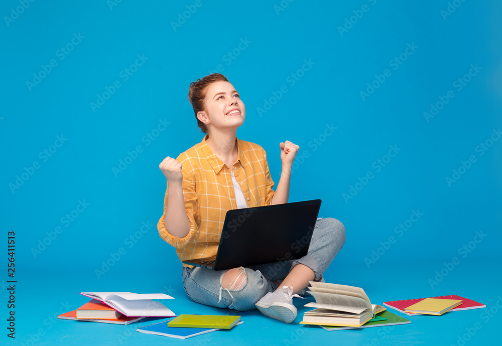 education, high school, technology and people concept - happy red haired teenage student girl in checkered shirt with books and laptop computer celebrating success over bright blue background