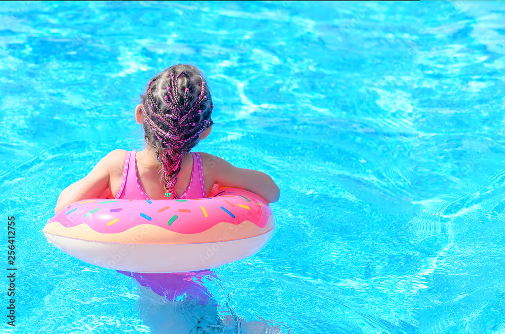 Cute little girl with inflatable donut ring in swimming pool on hot sunny day. Healthy and happy childhood concept. Back view