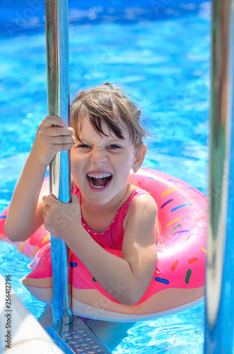 Cute laughing little girl with inflatable donut ring in swimming pool on hot sunny day. Healthy and happy childhood concept.