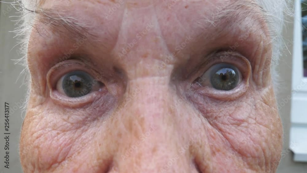 Close up wrinkled face of old grandmother looking into camera with a surprised expression. Portrait of mature woman strongly screwing up her gray eyes. Slow motion Close up wrinkled face of old grandmother looking into camera with a surprised expression. Portrait of mature woman strongly screwing up her gray eyes. Slow motion