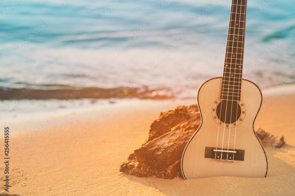 Fototapeta Guitar ukulele on sand beach with clear water and blue sky. Travel and lifestyle Concept.