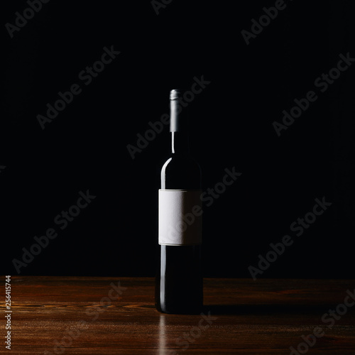 Wine bottle with blank label on wooden surface isolated on black