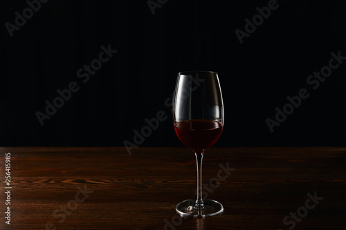 Glass of red wine on wooden surface isolated on black