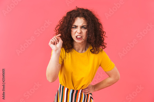 Angry beautiful young curly girl posing isolated over red wall background.