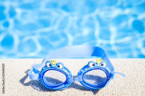 Closeup view of a boy blue swimming goggles on the pool edge with a big blue water copy space during a sunny summer day