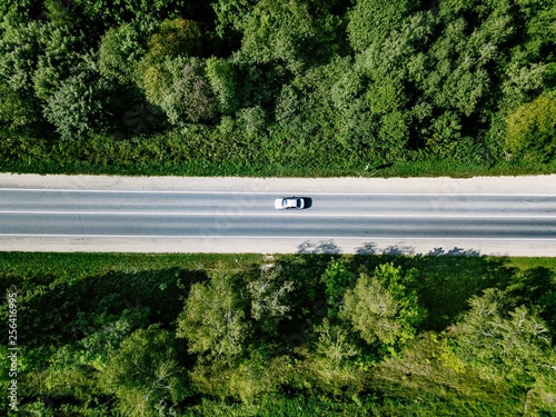 Aerial view of road with car going through green forest.