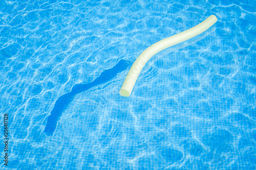 Closeup view of a yellow floating aid toy and its shadow on the blue water of the swimming pool during a sunny summer day