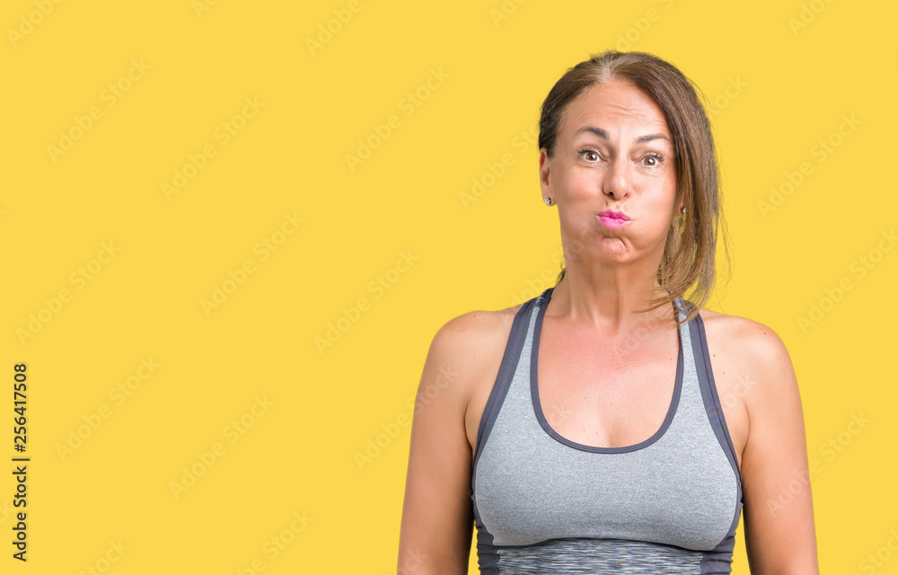 Beautiful middle age woman wearing sport clothes over isolated background puffing cheeks with funny face. Mouth inflated with air, crazy expression.
