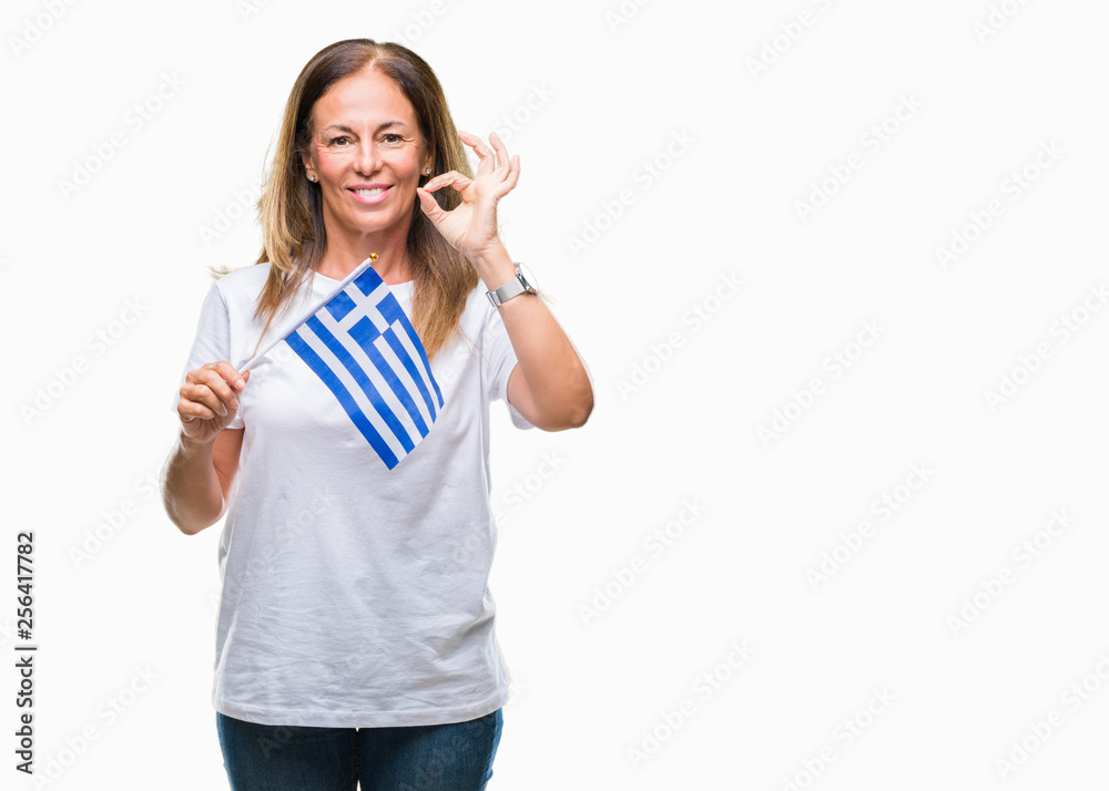 Middle age hispanic woman holding flag of Greece over isolated background doing ok sign with fingers, excellent symbol Middle age hispanic woman holding flag of Greece over isolated background doing ok sign with fingers, excellent symbol