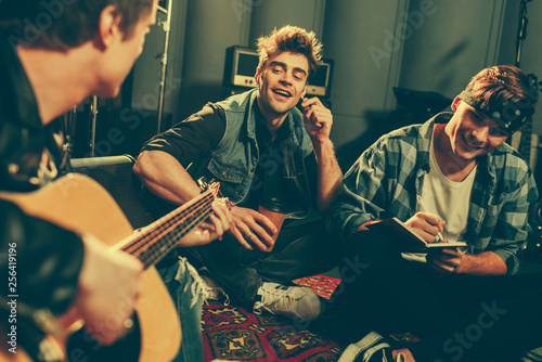 selective focus of cheerful friends looking at musician playing acoustic guitar