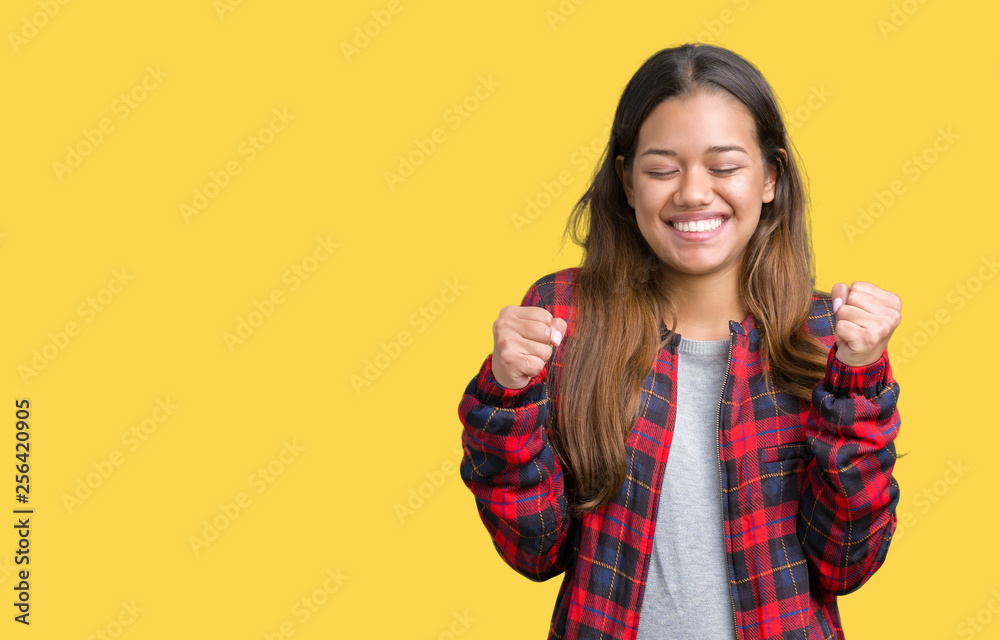 Young beautiful brunette woman wearing a jacket over isolated background excited for success with arms raised celebrating victory smiling. Winner concept. Young beautiful brunette woman wearing a jacket over isolated background excited for success with arms raised celebrating victory smiling. Winner concept.