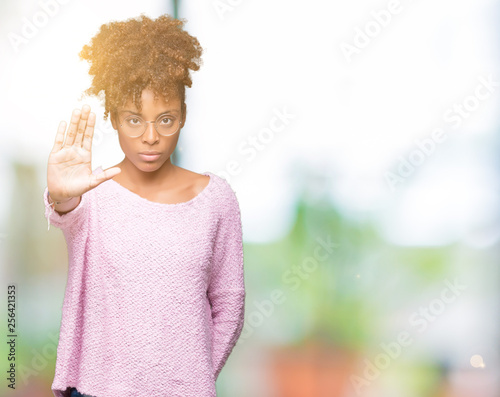 Beautiful young african american woman wearing glasses over isolated background doing stop sing with palm of the hand. Warning expression with negative and serious gesture on the face. © Krakenimages.com
