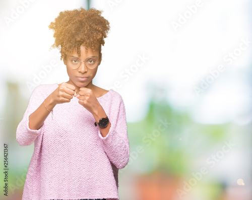 Beautiful young african american woman wearing glasses over isolated background Punching fist to fight, aggressive and angry attack, threat and violence © Krakenimages.com
