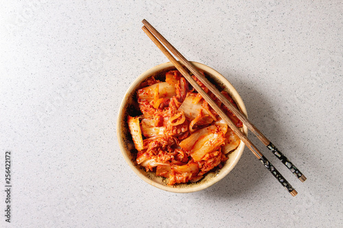 Obraz na płótnie Korean traditional fermented appetizer kimchi cabbage salad in ceramic bowl with shopsticks over grey spotted background