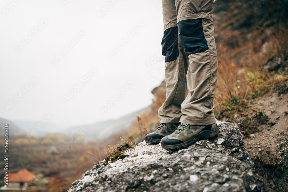 Outdoors cropped close up image of legs of young man hiking in mountains. Foots of traveler male standing on the rock during trekking. Travel, people and healthy lifestyle concept Outdoors cropped close up image of legs of young man hiking in mountains. Foots of traveler male standing on the rock during trekking. Travel, people and healthy lifestyle concept