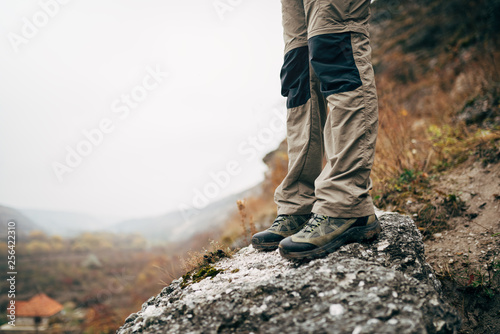 Outdoors cropped close up image of legs of young man hiking in mountains. Foots of traveler male standing on the rock during trekking. Travel, people and healthy lifestyle concept