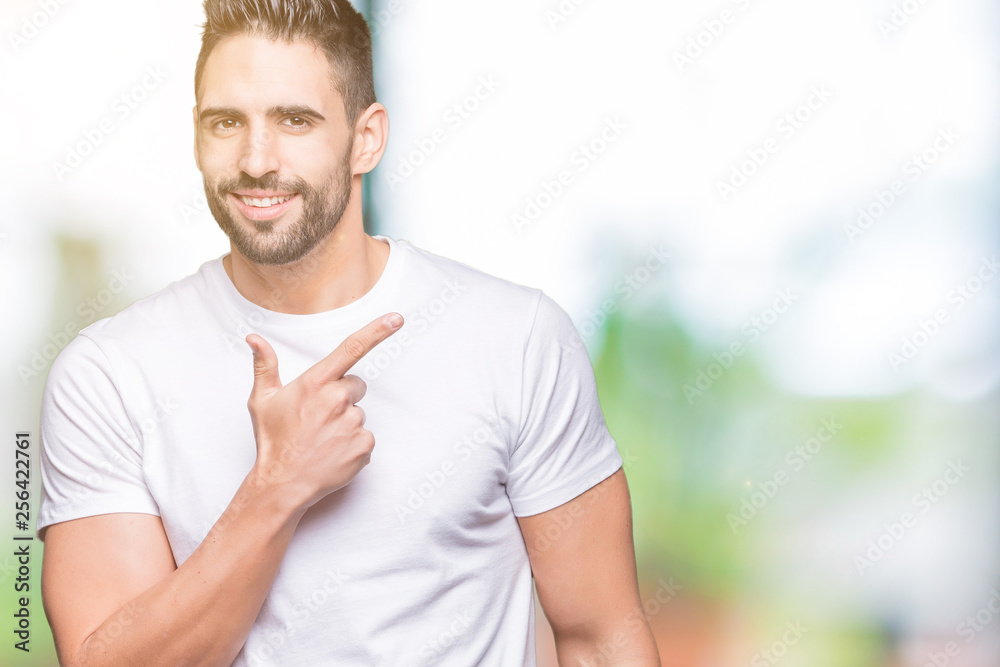 Young man wearing casual white t-shirt over isolated background cheerful with a smile of face pointing with hand and finger up to the side with happy and natural expression on face Young man wearing casual white t-shirt over isolated background cheerful with a smile of face pointing with hand and finger up to the side with happy and natural expression on face