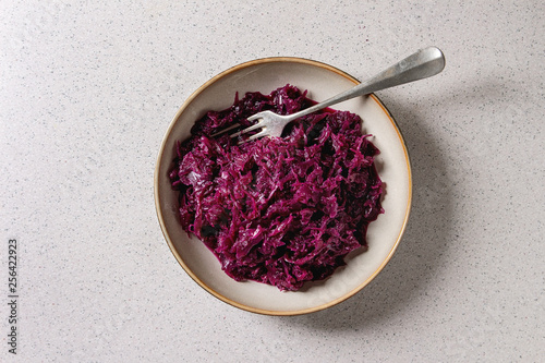 Red sauerkraut chopped cabbage pickled in brine with cumin in ceramic plate with fork over grey spotted background. Flat lay, space