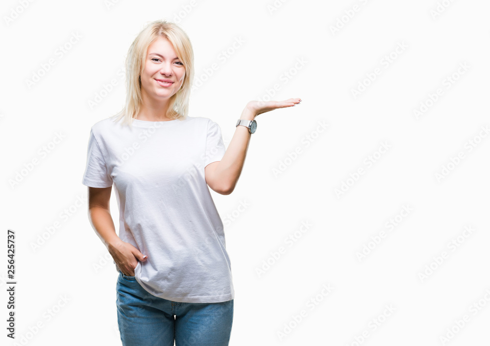 Young beautiful blonde woman wearing white t-shirt over isolated background smiling cheerful presenting and pointing with palm of hand looking at the camera. Young beautiful blonde woman wearing white t-shirt over isolated background smiling cheerful presenting and pointing with palm of hand looking at the camera.