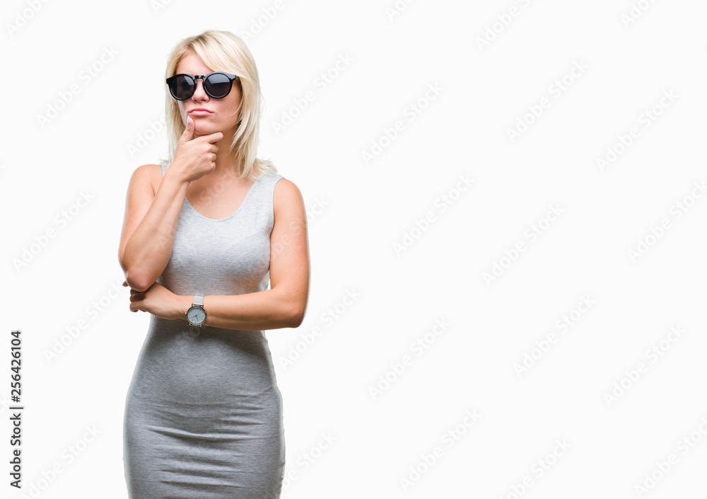 Young beautiful blonde woman wearing sunglasses over isolated background with hand on chin thinking about question, pensive expression. Smiling with thoughtful face. Doubt concept. Young beautiful blonde woman wearing sunglasses over isolated background with hand on chin thinking about question, pensive expression. Smiling with thoughtful face. Doubt concept.