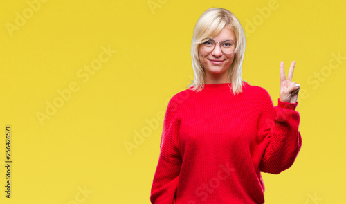 Young beautiful blonde woman wearing sweater and glasses over isolated background showing and pointing up with fingers number two while smiling confident and happy.