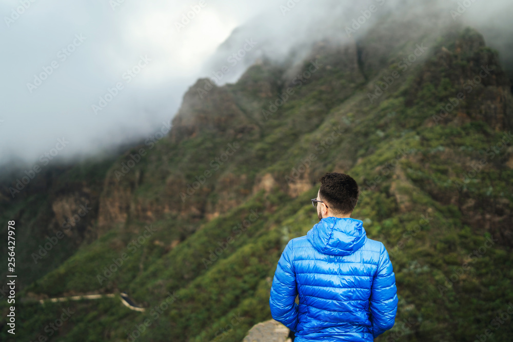 Man in blue jacket relaxing in the mountains with cloudy sky