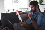 Young bearded businessman  working on laptop computer while sitting on sofa at home