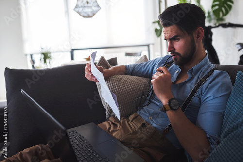 Young bearded businessman  working on laptop computer while sitting on sofa at home