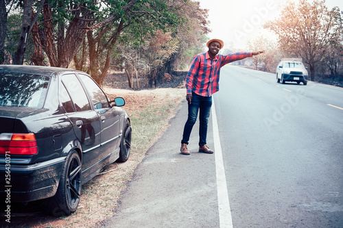 African man raising hands for help because his car is broken side the highway