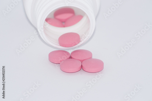 pink pills on white background fall out of a plastic jar