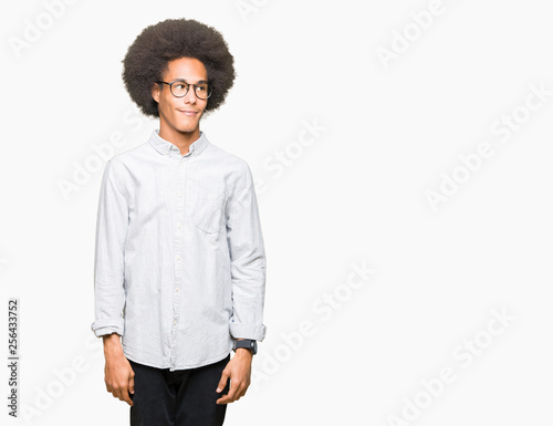 Young african american man with afro hair wearing glasses looking away to side with smile on face, natural expression. Laughing confident.