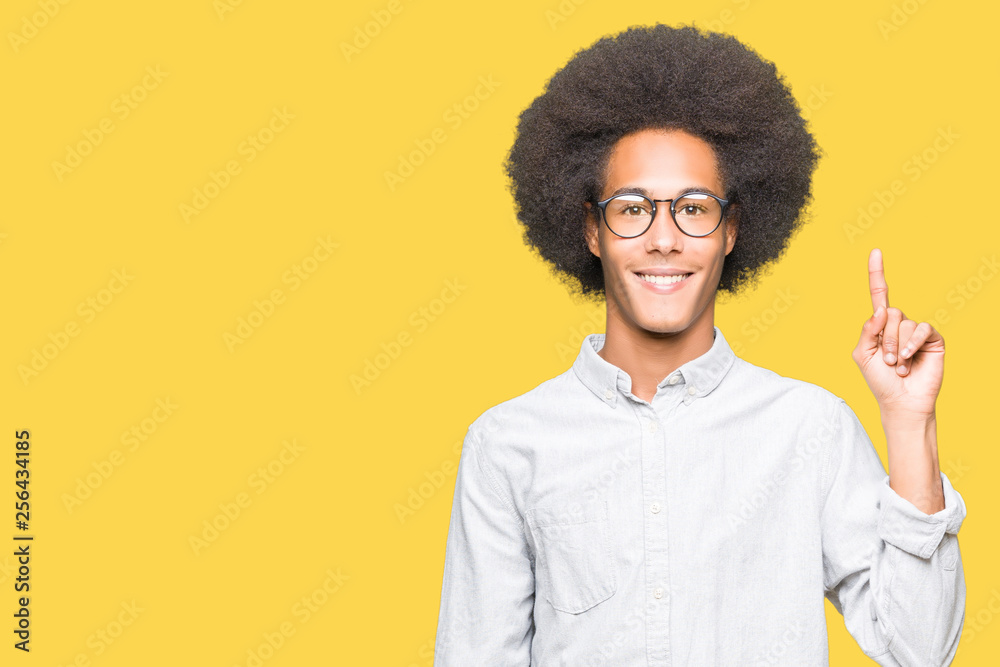 Young african american man with afro hair wearing glasses showing and pointing up with finger number one while smiling confident and happy. Young african american man with afro hair wearing glasses showing and pointing up with finger number one while smiling confident and happy.
