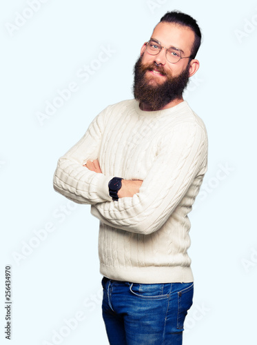 Young hipster man wearing glasses and winter sweater happy face smiling with crossed arms looking at the camera. Positive person.