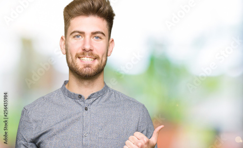 Young handsome business casual man doing happy thumbs up gesture with hand. Approving expression looking at the camera with showing success.