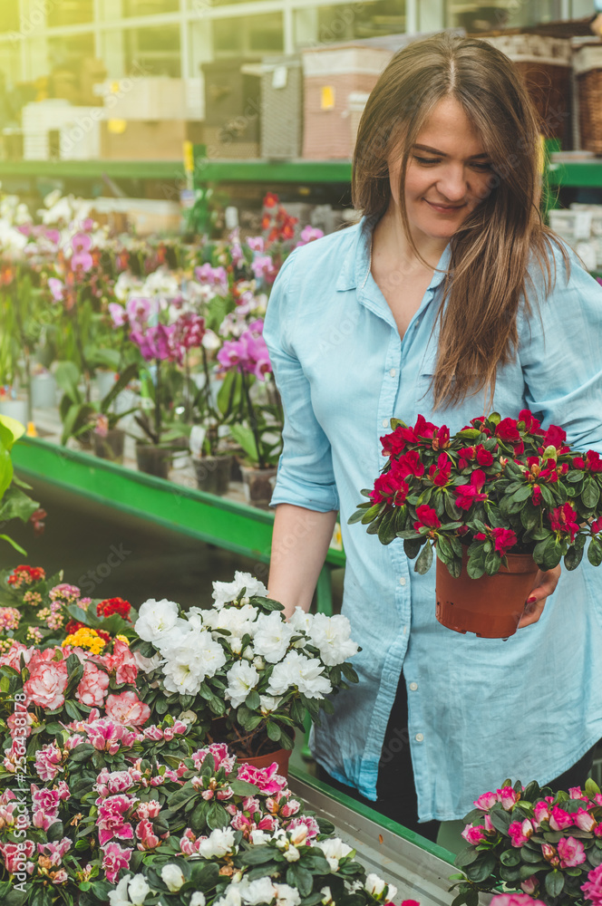 Beautiful female customer smelling colorful blooming flowerpots in the retail store. 