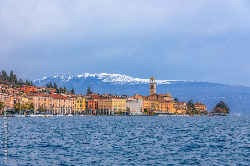 Panoramic view of the city Salo (Salò) and the embankment on Lake Garda. In the background are snowy Alps. Winter period.  Lombardy region, Italy