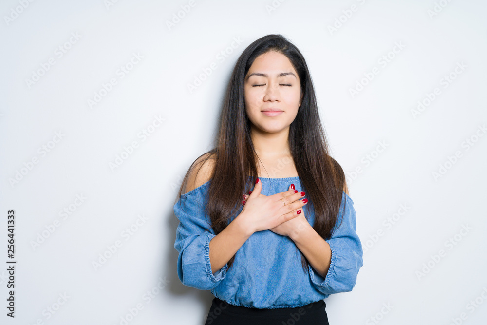 Beautiful brunette woman over isolated background smiling with hands on chest with closed eyes and grateful gesture on face. Health concept. Beautiful brunette woman over isolated background smiling with hands on chest with closed eyes and grateful gesture on face. Health concept.