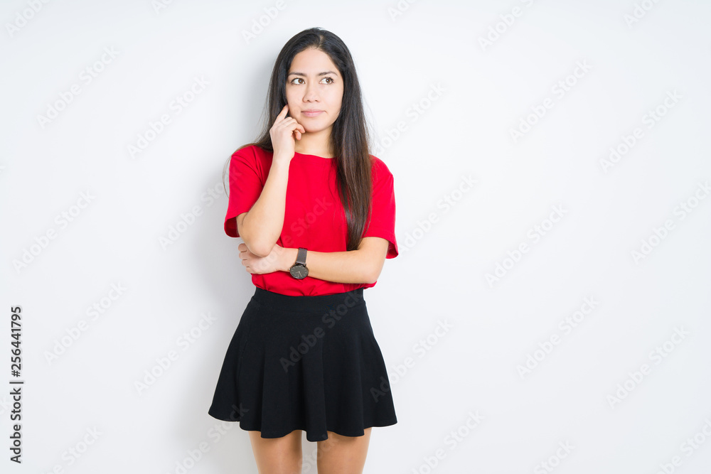 Beautiful brunette woman wearing red t-shirt and skirt over isolated background with hand on chin thinking about question, pensive expression. Smiling with thoughtful face. Doubt concept. Beautiful brunette woman wearing red t-shirt and skirt over isolated background with hand on chin thinking about question, pensive expression. Smiling with thoughtful face. Doubt concept.