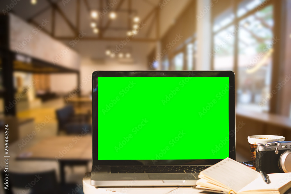 Mockup image of laptop with blank green screen with camera,notebook,coffee cup on wooden table of In the coffee shop background. Mockup image of laptop with blank green screen with camera,notebook,coffee cup on wooden table of In the coffee shop background.