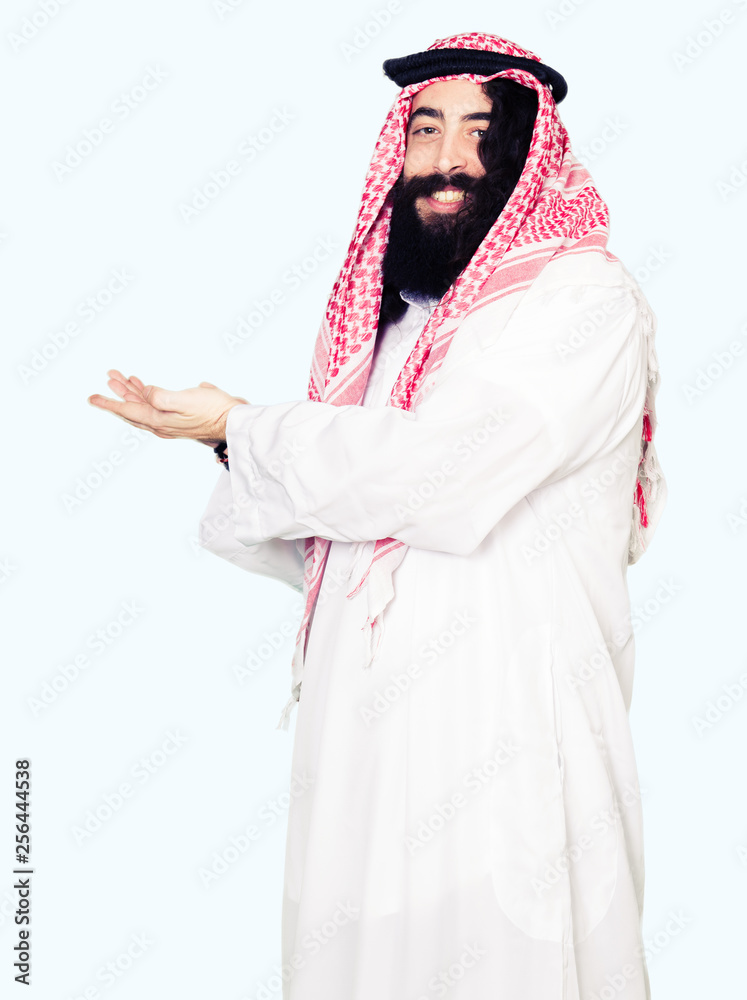 Arabian business man with long hair wearing traditional keffiyeh scarf Pointing to the side with hand and open palm, presenting ad smiling happy and confident Arabian business man with long hair wearing traditional keffiyeh scarf Pointing to the side with hand and open palm, presenting ad smiling happy and confident