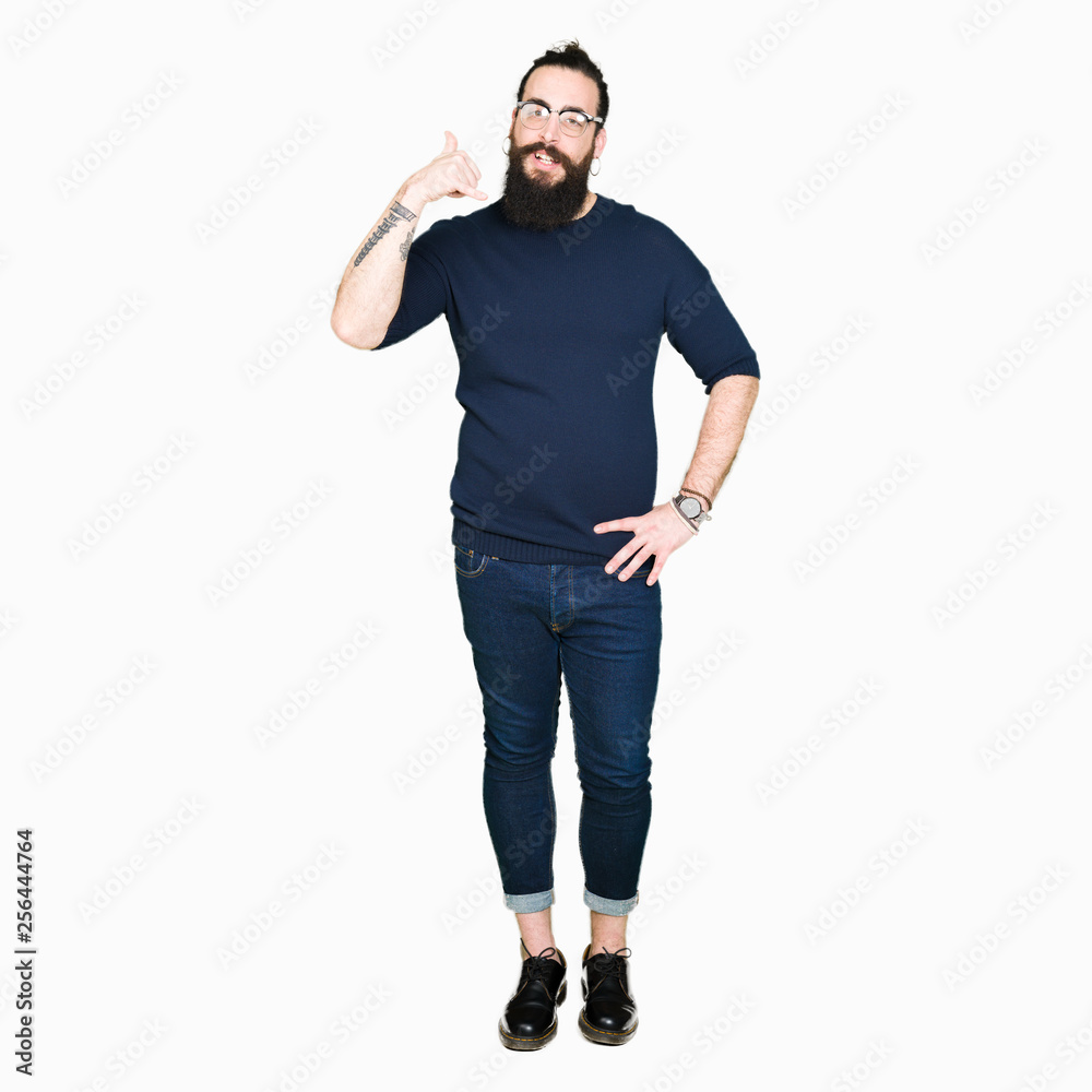 Young hipster man with long hair and beard wearing glasses smiling doing phone gesture with hand and fingers like talking on the telephone. Communicating concepts. Young hipster man with long hair and beard wearing glasses smiling doing phone gesture with hand and fingers like talking on the telephone. Communicating concepts.