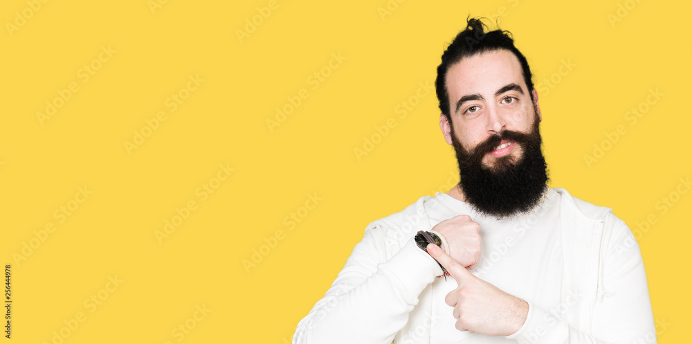 Fototapeta premium Young hipster man with long hair and beard wearing sporty sweatshirt In hurry pointing to watch time, impatience, upset and angry for deadline delay