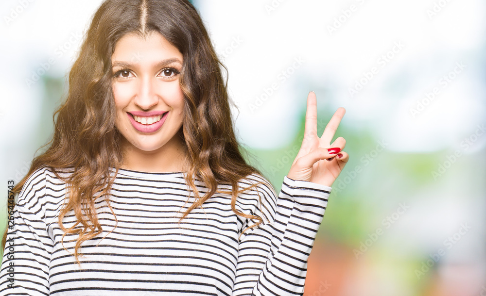 Young beautiful woman wearing stripes sweater smiling with happy face winking at the camera doing victory sign. Number two. Young beautiful woman wearing stripes sweater smiling with happy face winking at the camera doing victory sign. Number two.