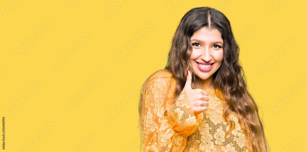 Young beautiful woman wearing yellow elegant dress doing happy thumbs up gesture with hand. Approving expression looking at the camera with showing success. Young beautiful woman wearing yellow elegant dress doing happy thumbs up gesture with hand. Approving expression looking at the camera with showing success.