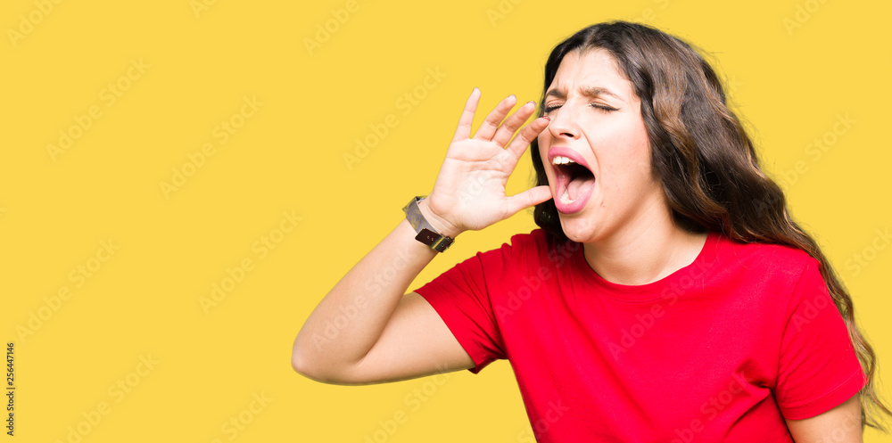 Young beautiful woman wearing casual t-shirt shouting and screaming loud to side with hand on mouth. Communication concept. Young beautiful woman wearing casual t-shirt shouting and screaming loud to side with hand on mouth. Communication concept.