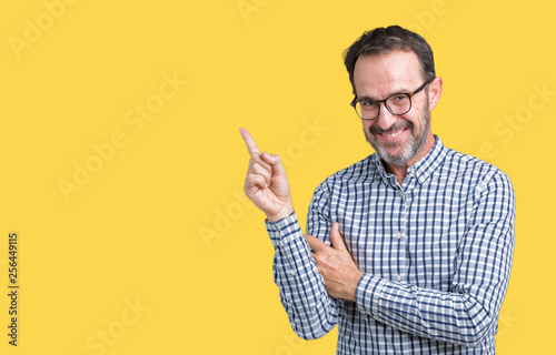 Handsome middle age elegant senior business man wearing glasses over isolated background with a big smile on face, pointing with hand and finger to the side looking at the camera.