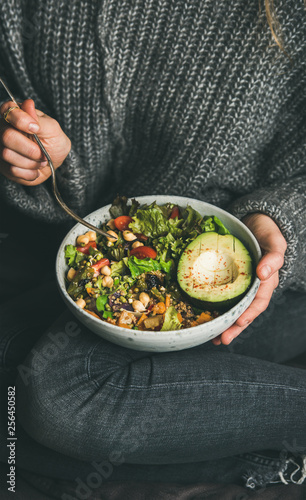 Healthy vegetarian dinner. Woman in jeans and warm woolen sweater holding bowl with fresh salad, avocado, grains, beans, roasted vegetables. Superfood, clean eating, vegan, dieting food concept