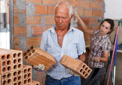 Elderly man with daughter installing brick wall inside