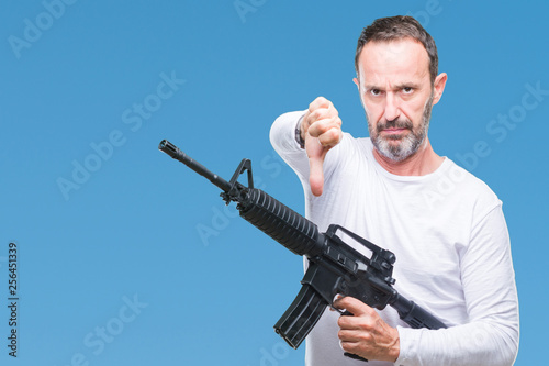 Middle age senior hoary criminal man holding gun weapon over isolated background with angry face  negative sign showing dislike with thumbs down  rejection concept